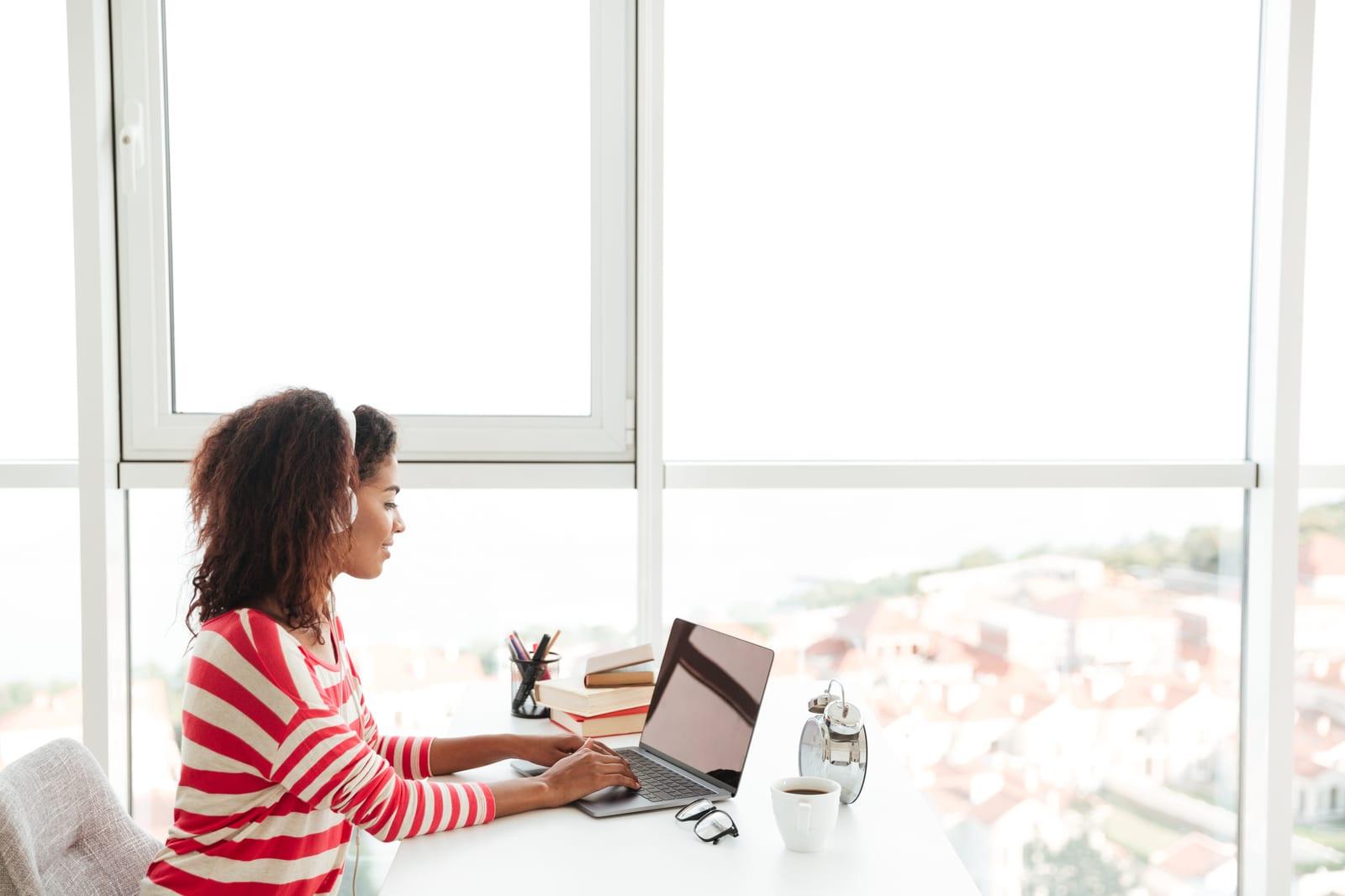 Young confident african woman in headphones working on laptop